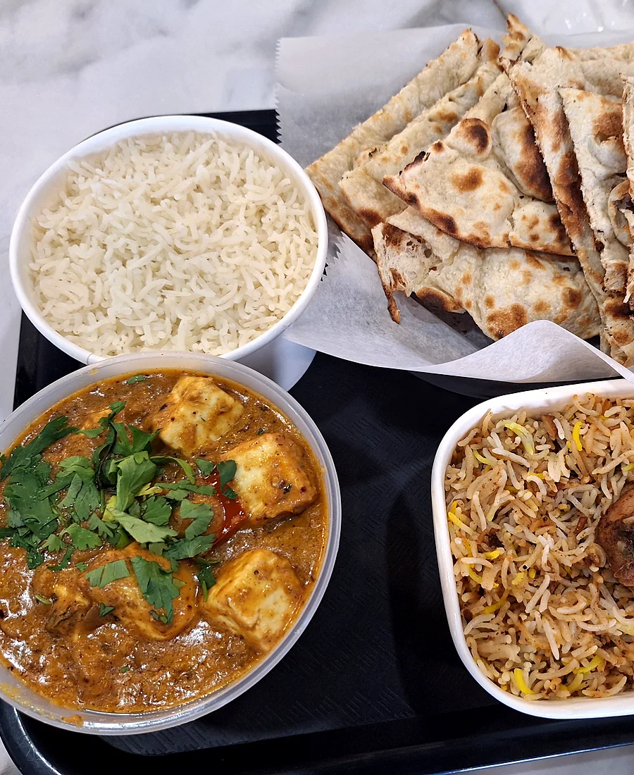Takeout meal of paneer curry, biryani, rice and naan on a tray