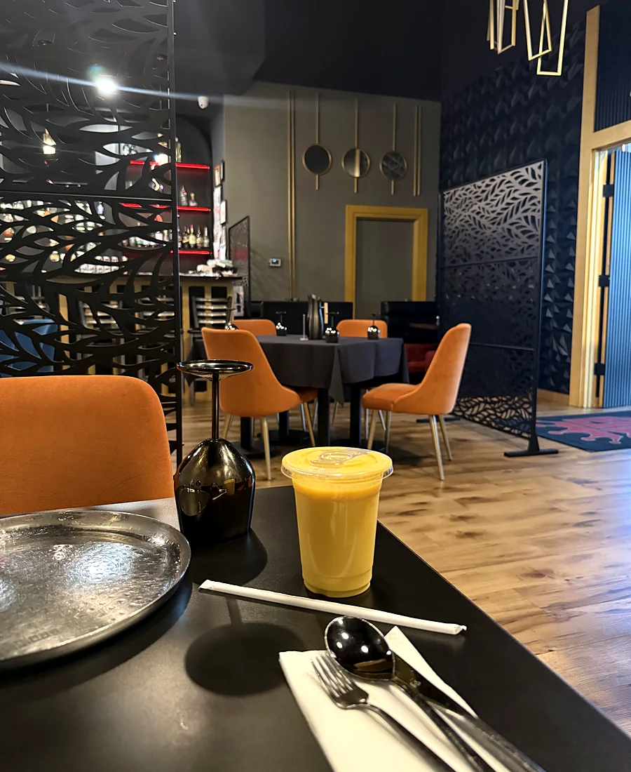 Table set with a steel plate and a glass of juice beside a carved screen and orange chairs